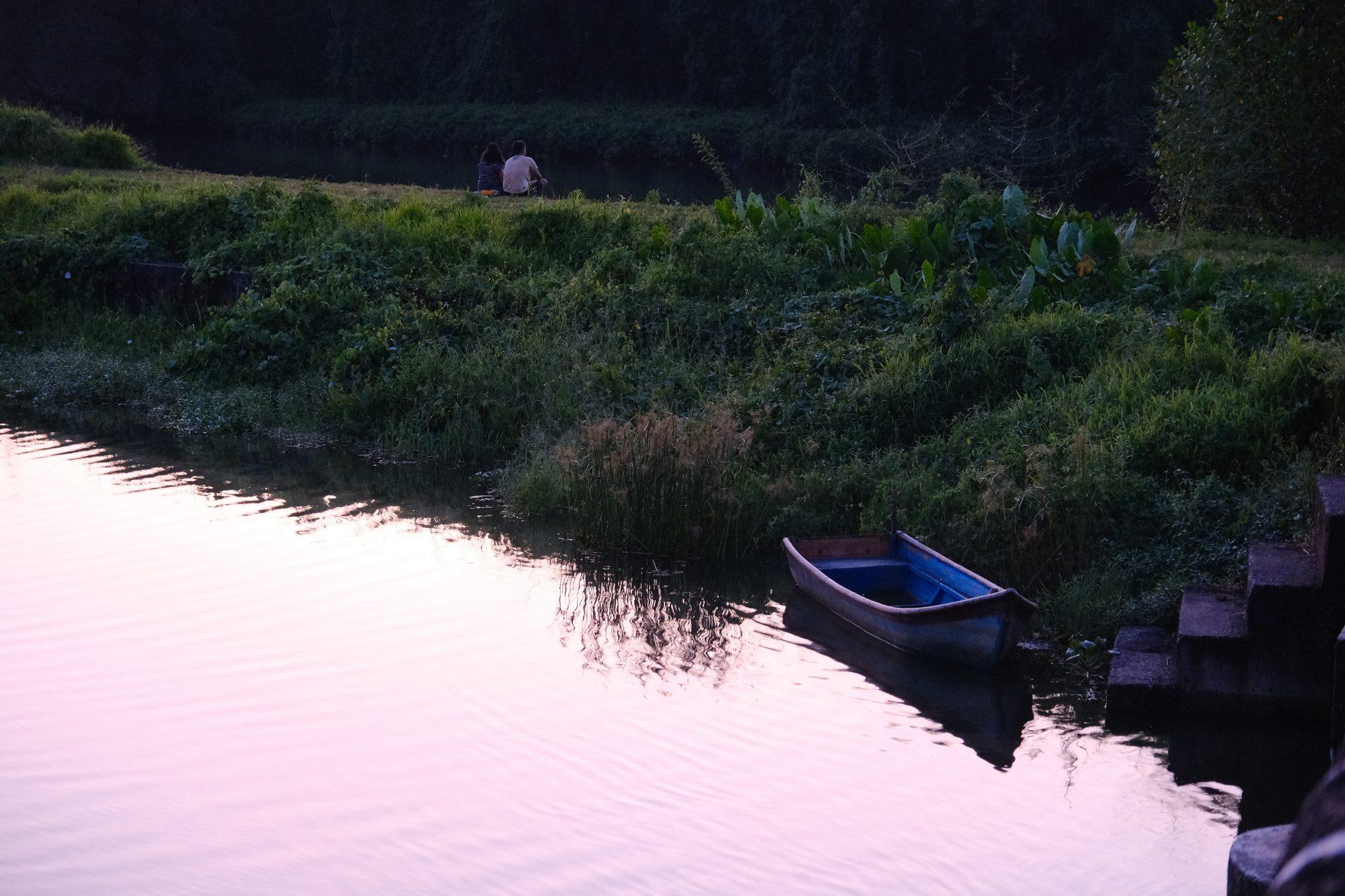 A moored wooden boat on water turned pink by the dusk sky