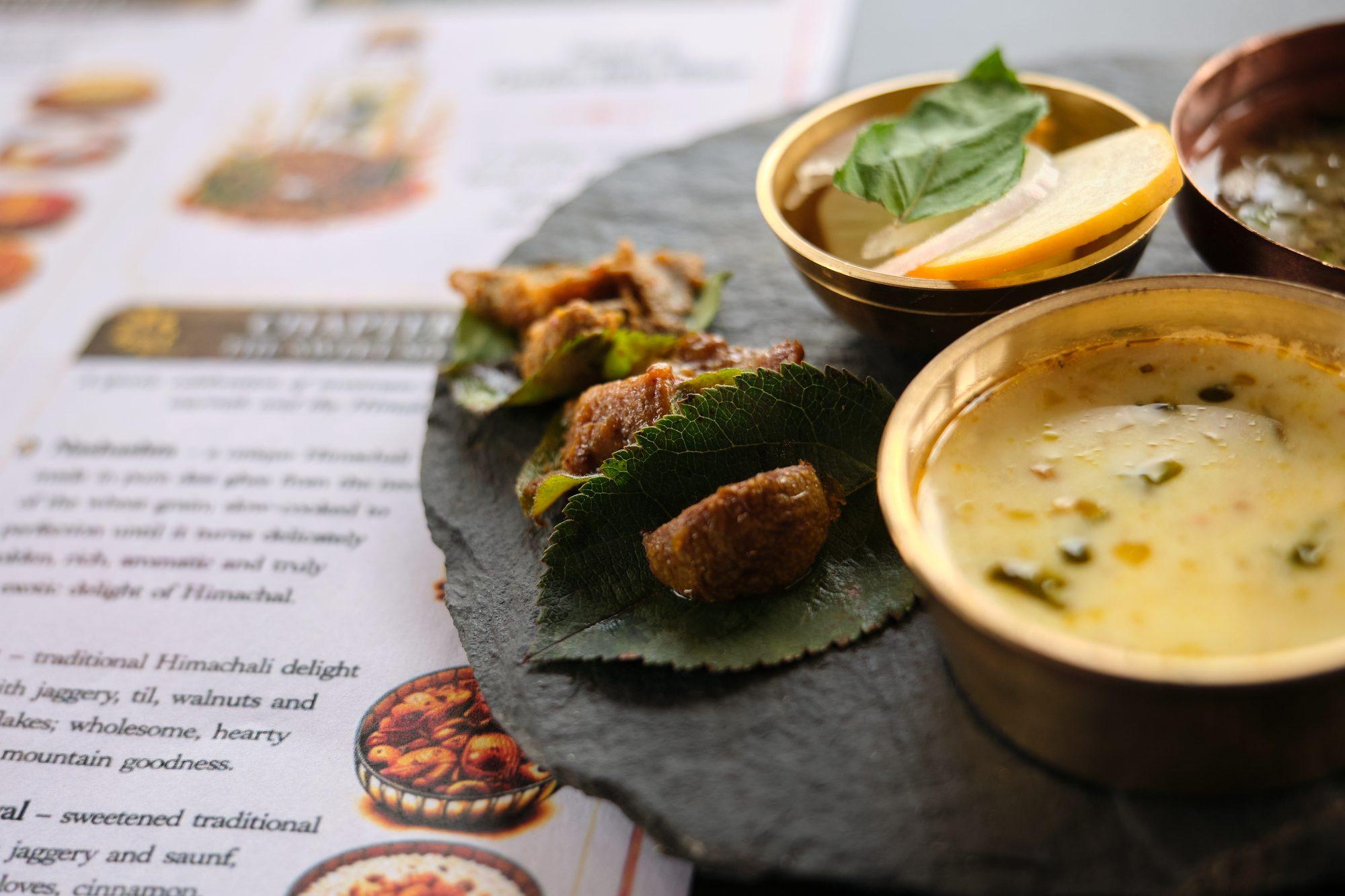 Brass katoris and a slate platter on the illustrated tasting menu