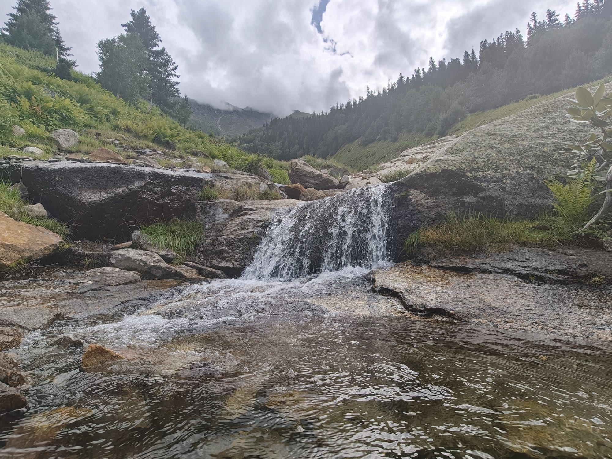 A waterfall dropping over a dark slab into a clear pool