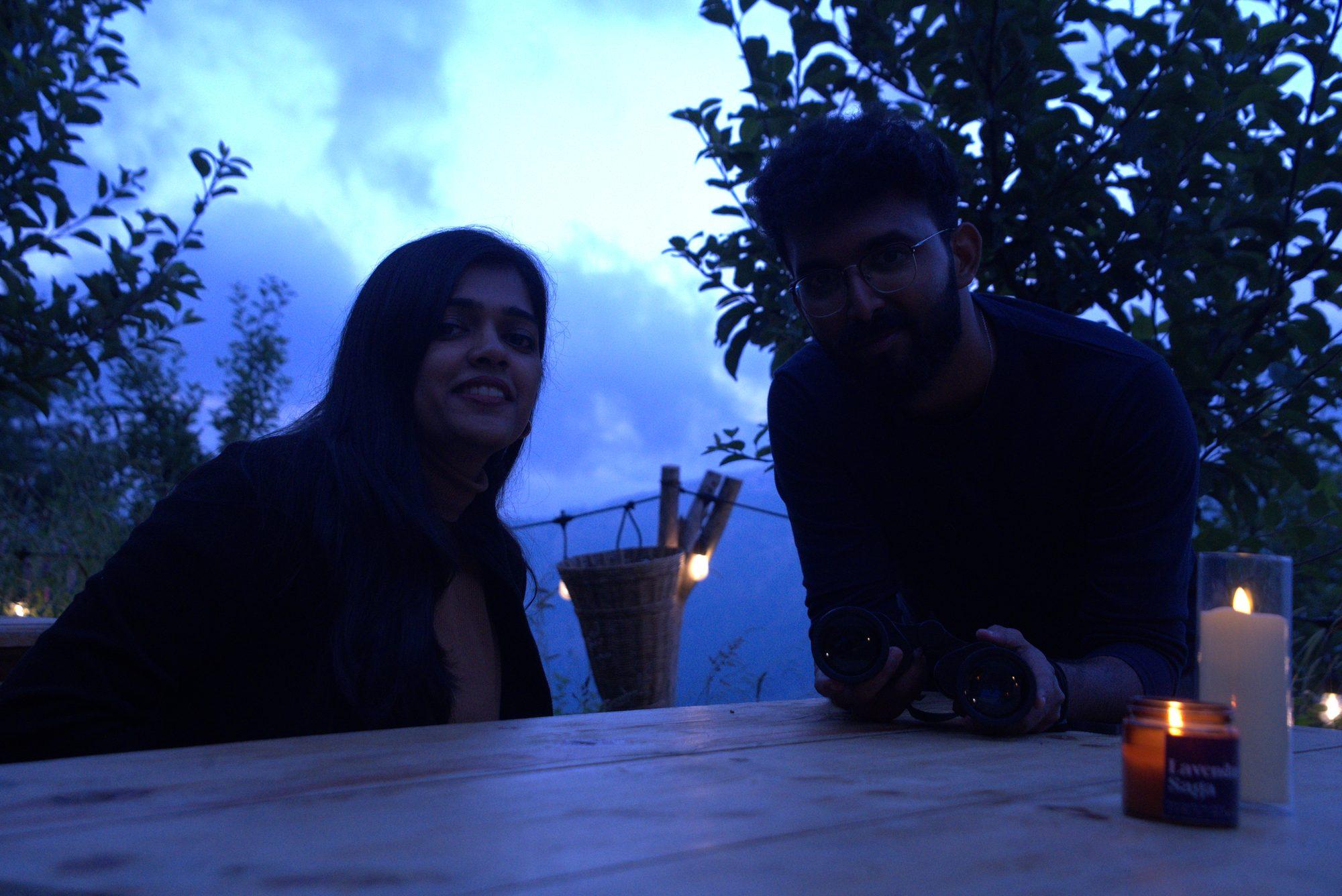 A couple at a candlelit table in the orchard as the light goes