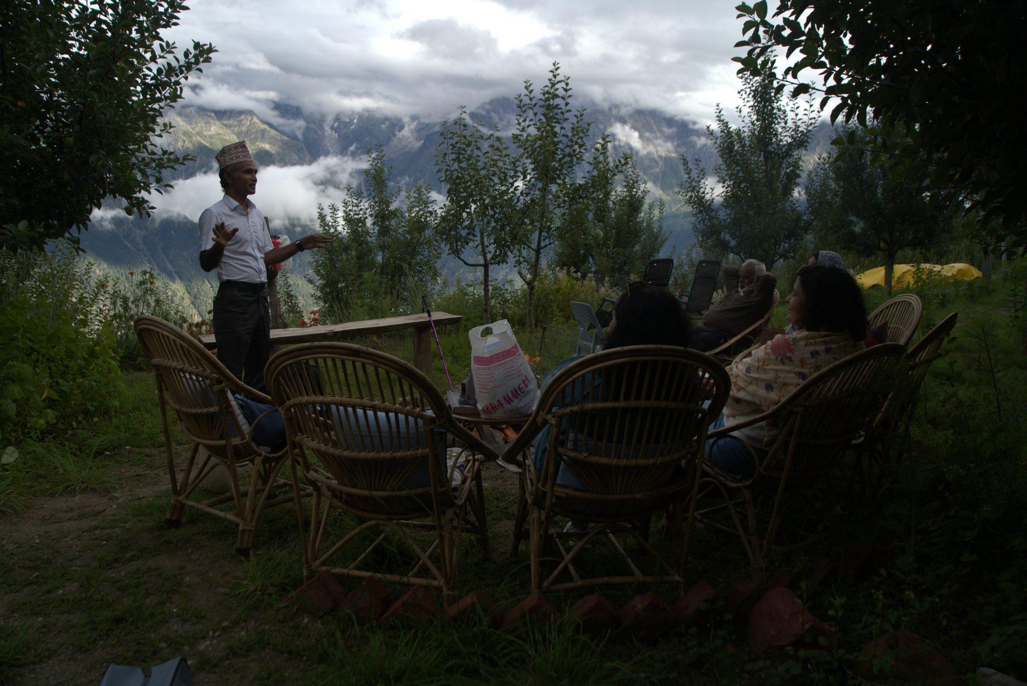 The host pouring for guests in cane chairs at the orchard edge