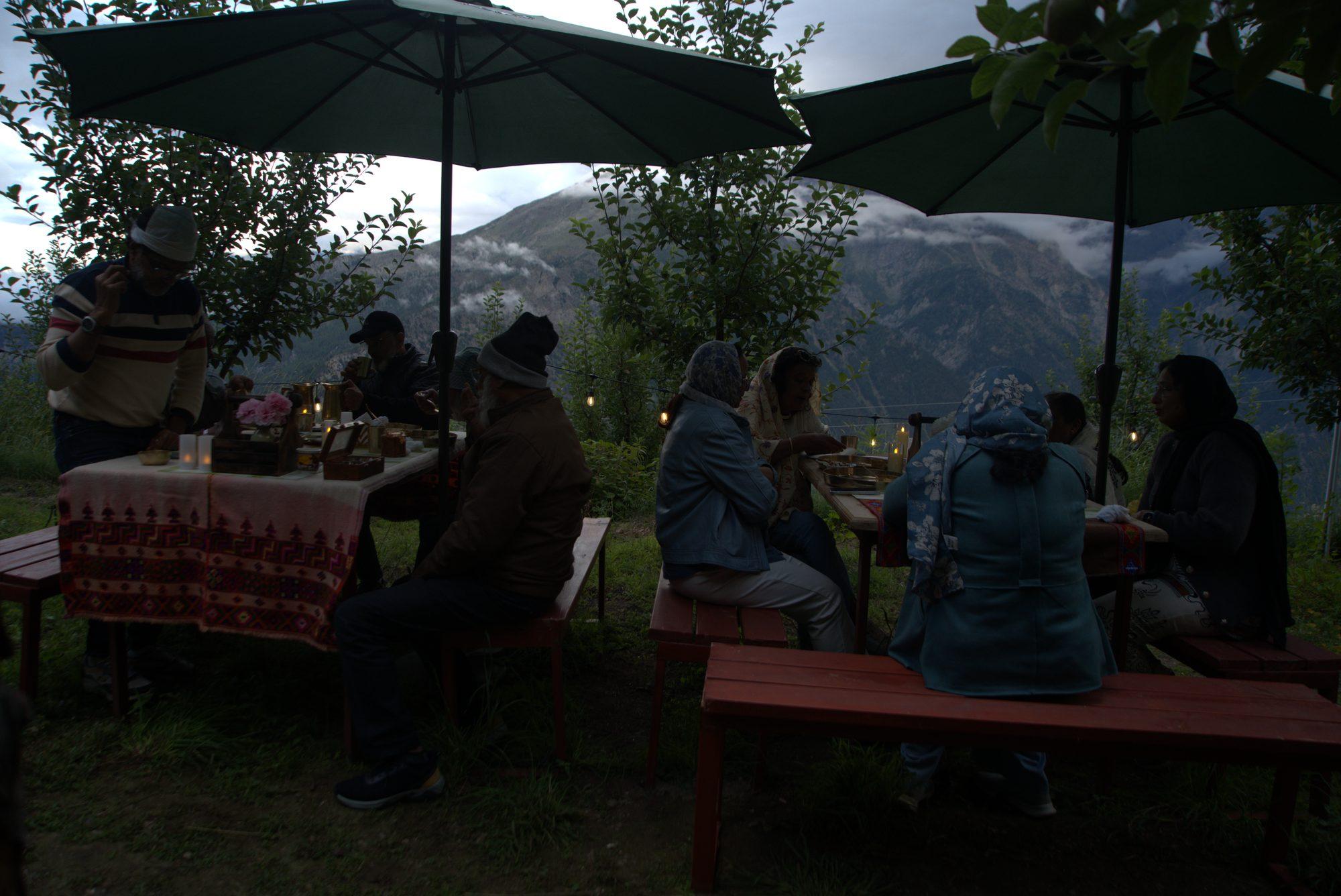 Guests at the long table under a green parasol with the valley beyond
