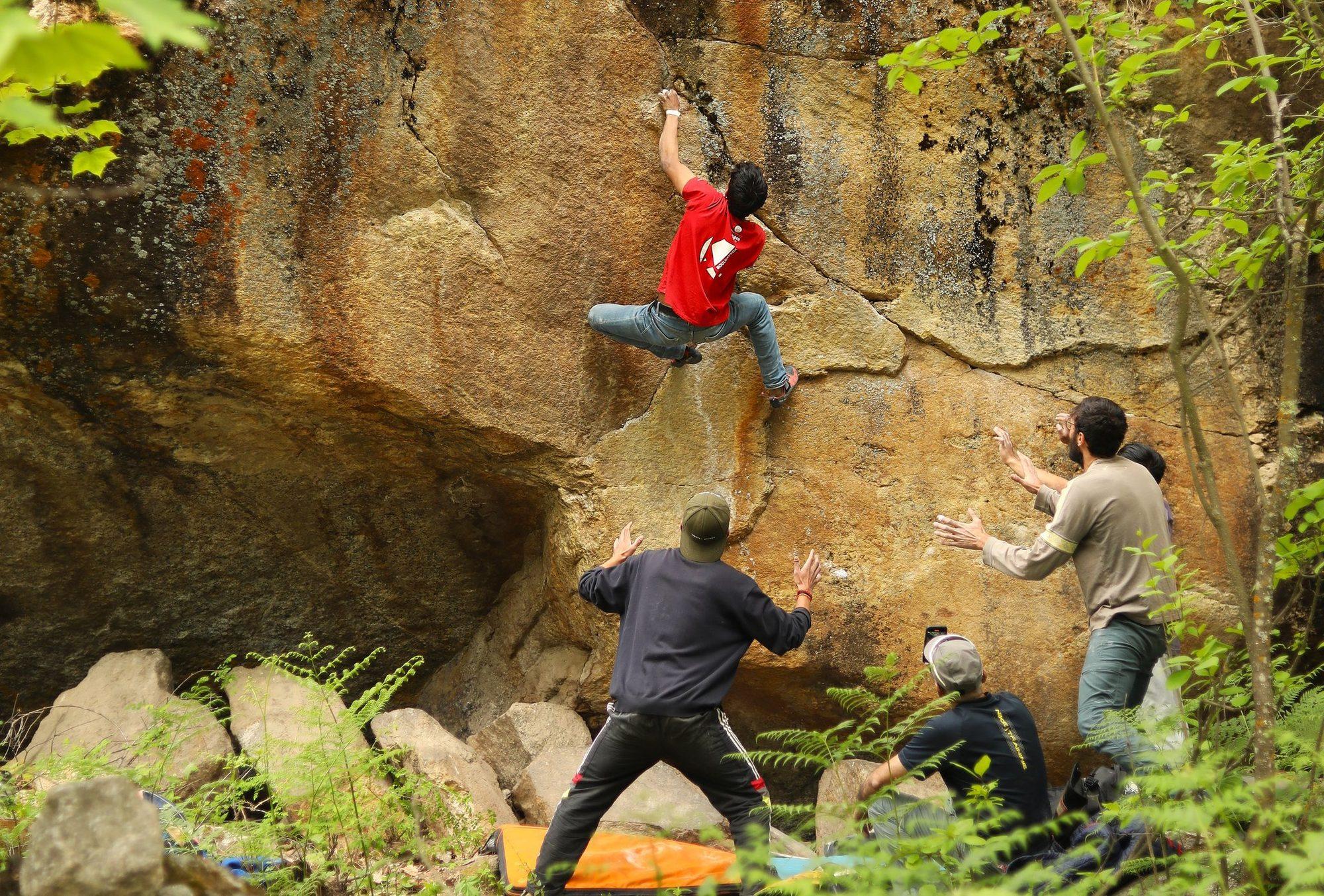 A climber on the boulder with three spotters below