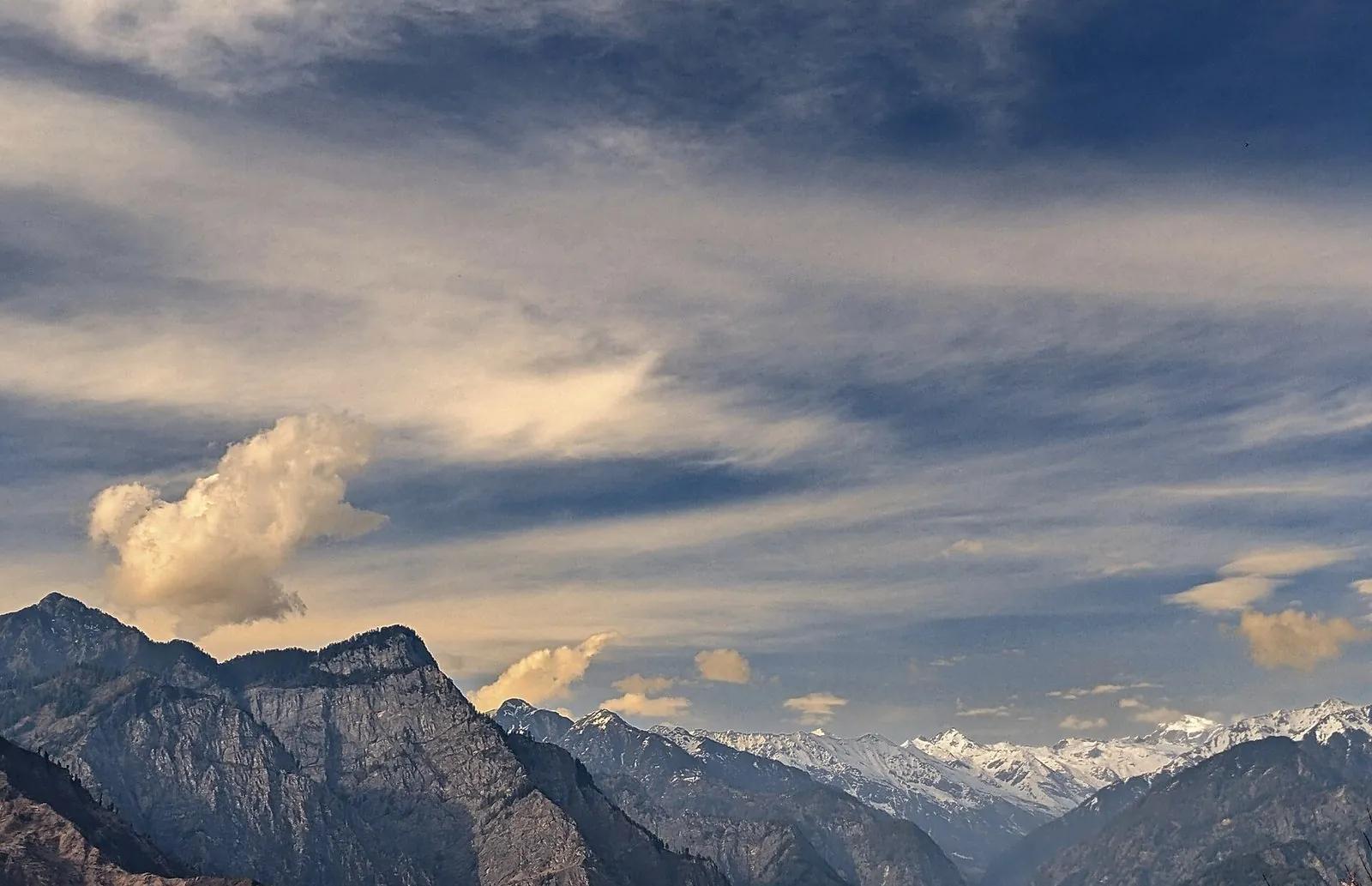 Parvati Valley panorama — layered Himalayan peaks under a dramatic cloud-scape, snow-line visible in the distance