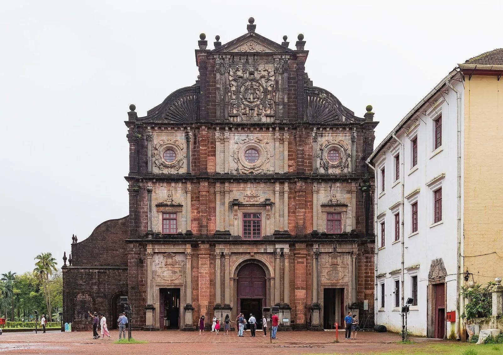 The bare laterite-stone Baroque front elevation of the Basilica of Bom Jesus in Old Goa, three tiers of carved facade with people small at the entrance