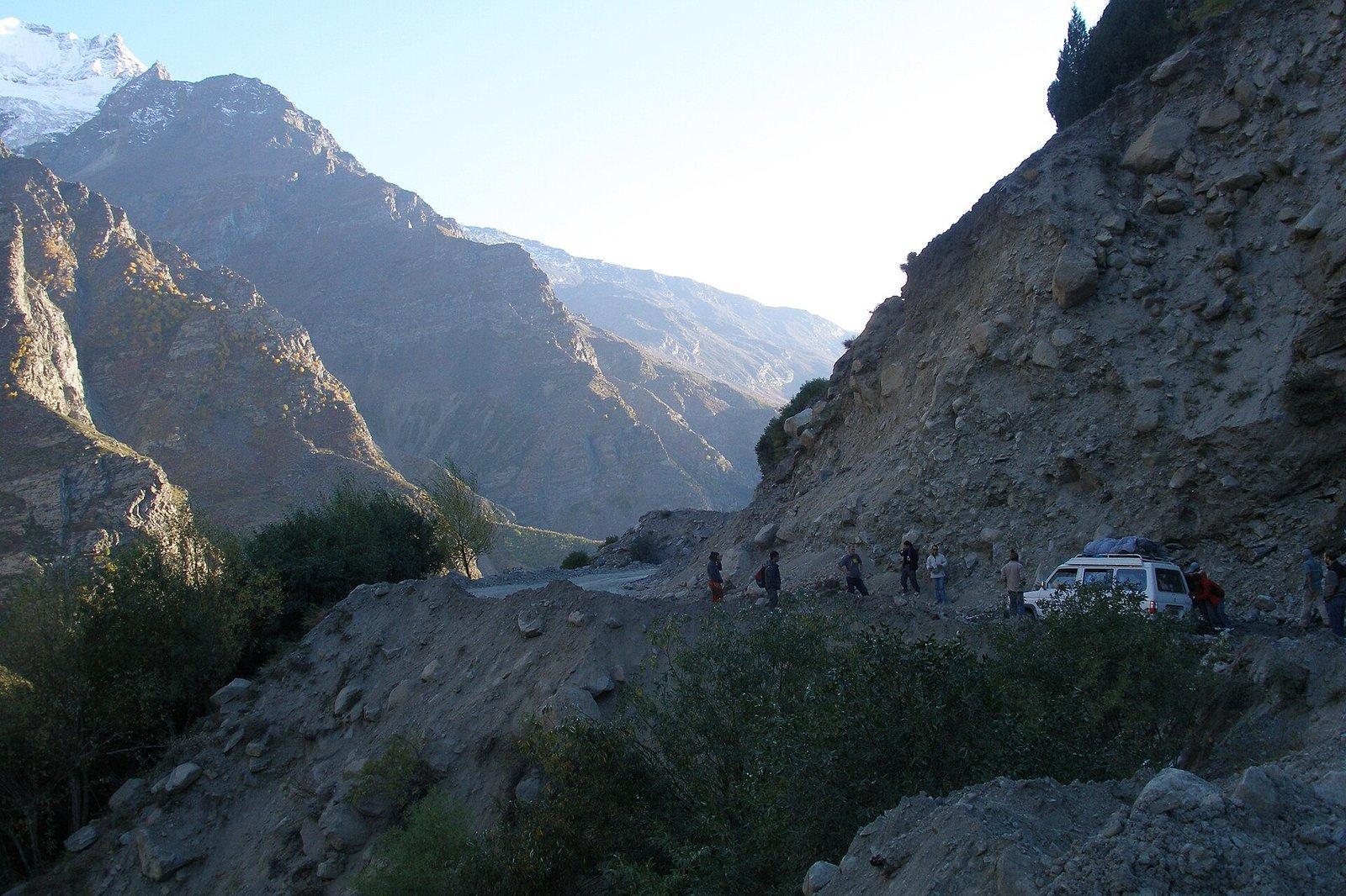 Narrow mountain road carved into a steep Himalayan gorge in Himachal Pradesh with vehicles navigating rough terrain