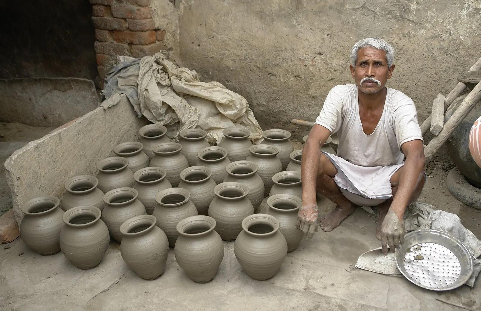 A village potter squatting beside rows of freshly thrown grey clay water pots