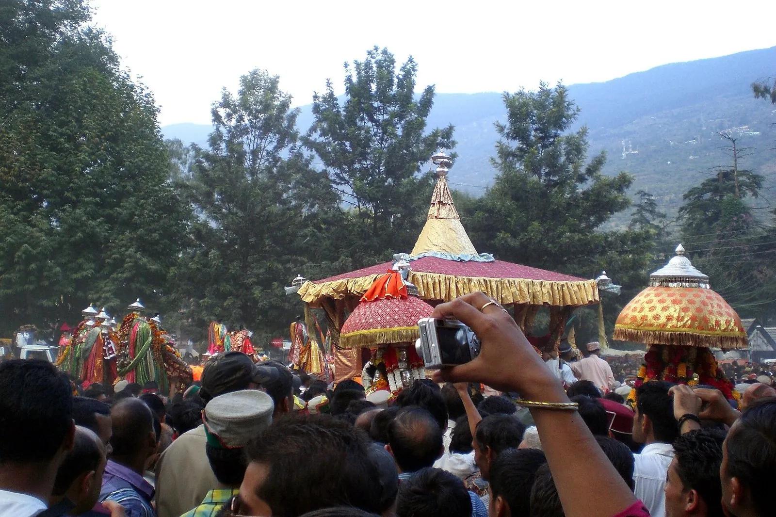 Decorated deity palanquins under gold canopies carried through the crowd at Kullu Dussehra, Dhalpur