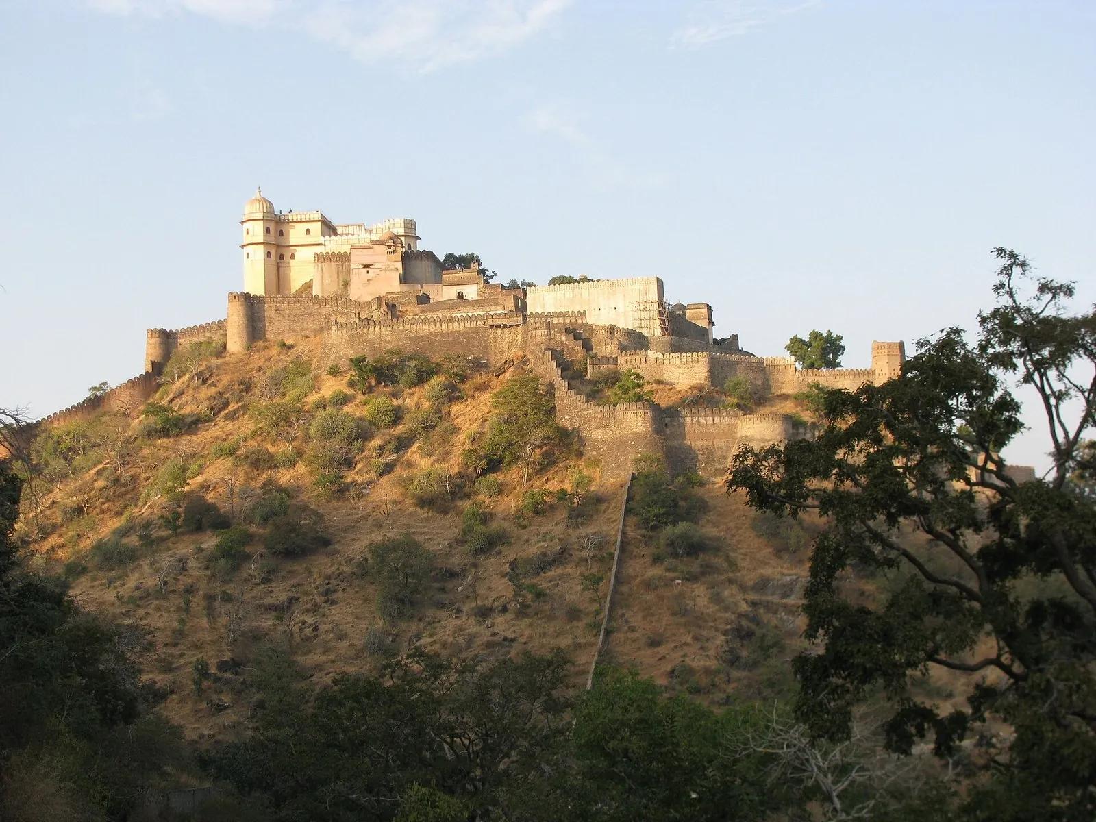 Kumbhalgarh Fort on a hilltop at sunset near Udaipur, its crenellated stone wall running down the Aravalli ridge in warm evening light.