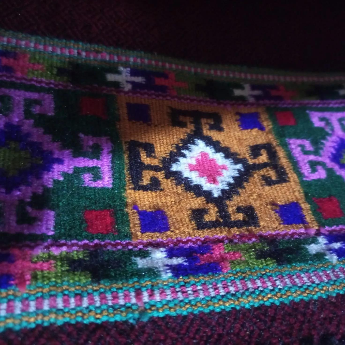 Close-up of a Himachali handwoven shawl border, dense geometric patti motifs in purple, green, gold and red on a maroon ground