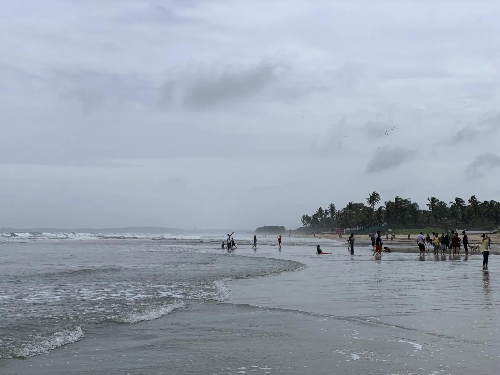 Wide Colva beach in South Goa beneath a heavy overcast sky with small groups near the shoreline