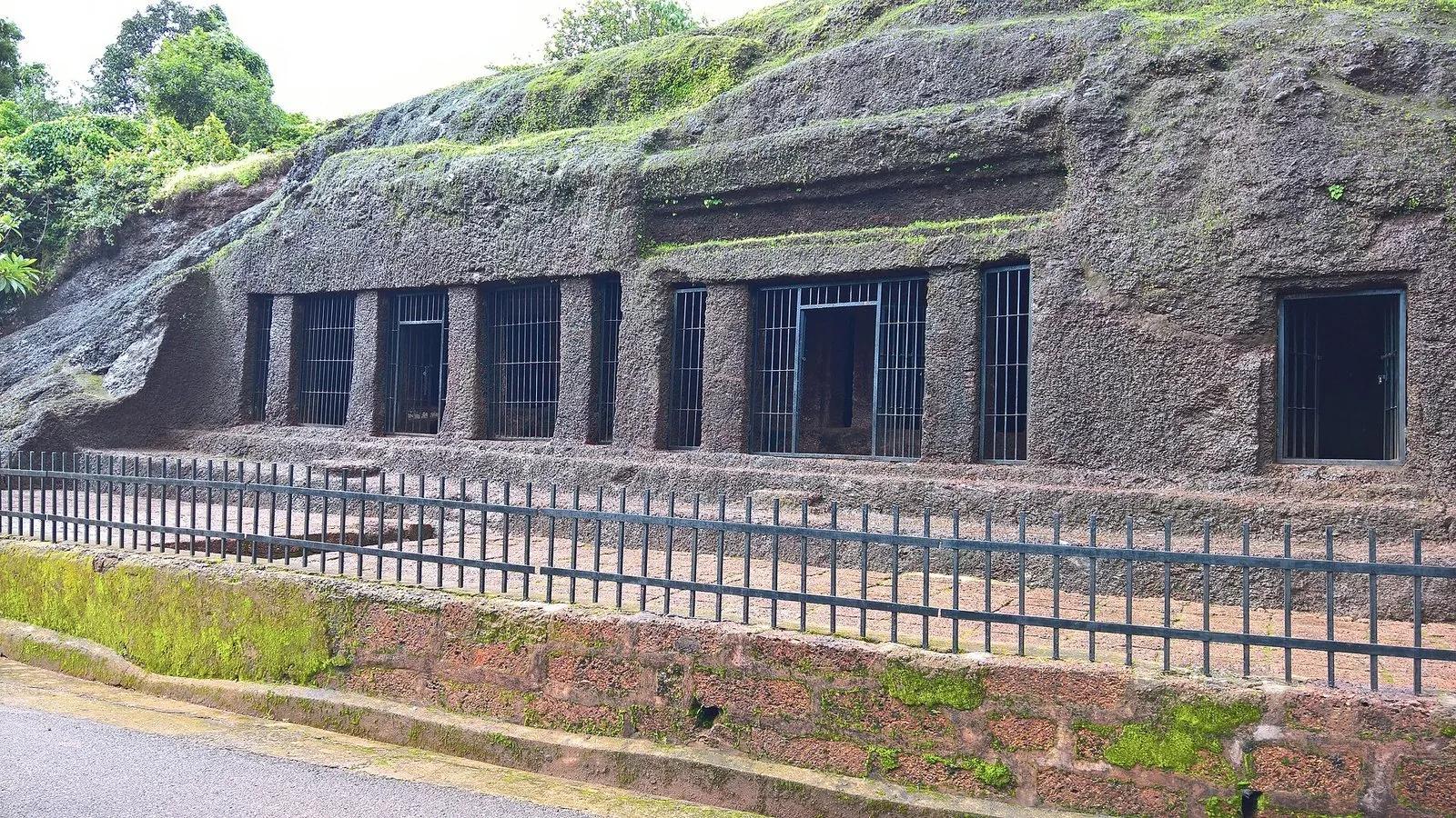 A row of rock-cut cave chambers with barred gates cut into a laterite hillside at Arvalem, Goa