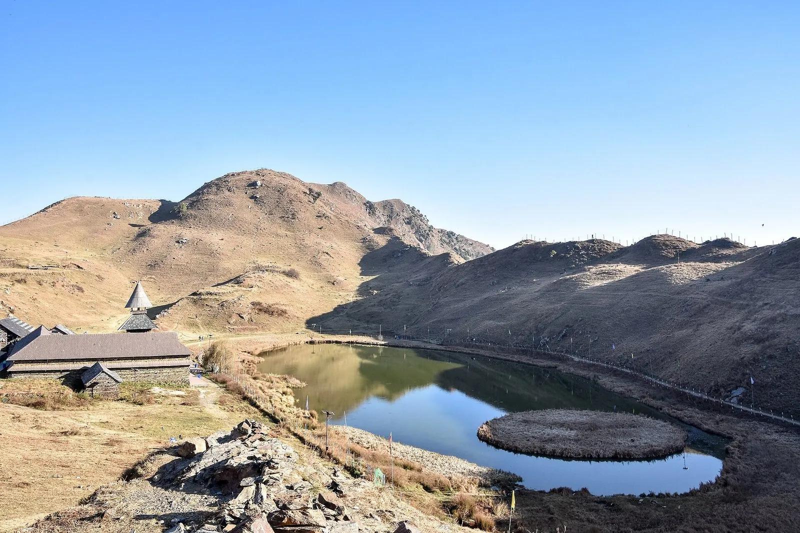 Prashar Lake at 2730 metres with the floating vegetation island visible in the centre and the three-tiered pagoda temple of Sage Parashar on the western shore