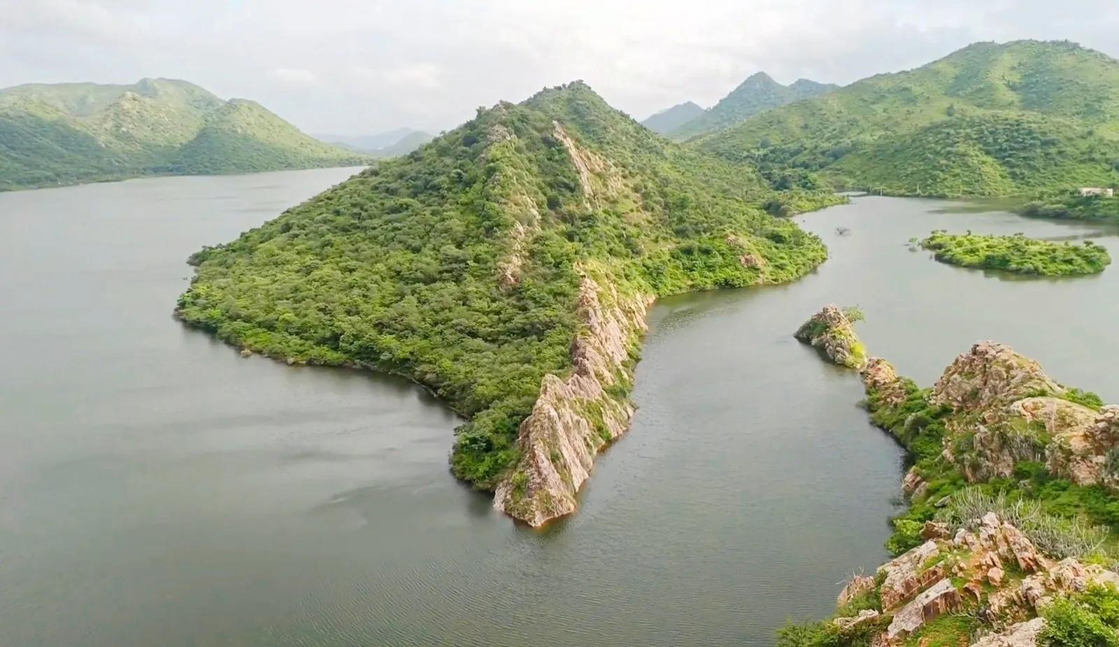 Bahubali Hills near Udaipur: green Aravalli hills and a pyramid-shaped forested ridge surrounded by the calm water of Badi Lake in the monsoon.