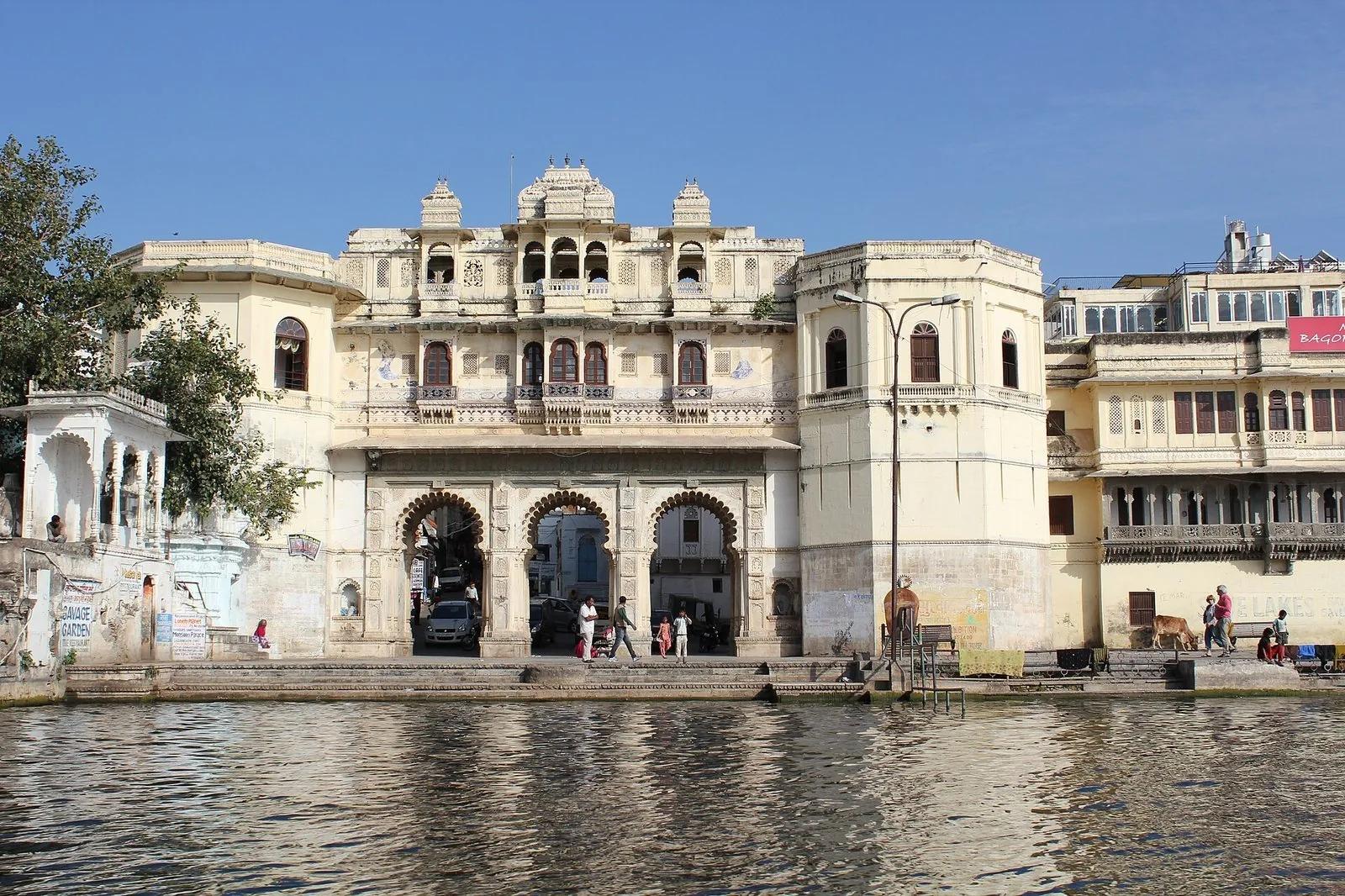 The Lal Ghat waterfront on Lake Pichola in Udaipur, a heritage haveli rising from the water with people on the ghat steps