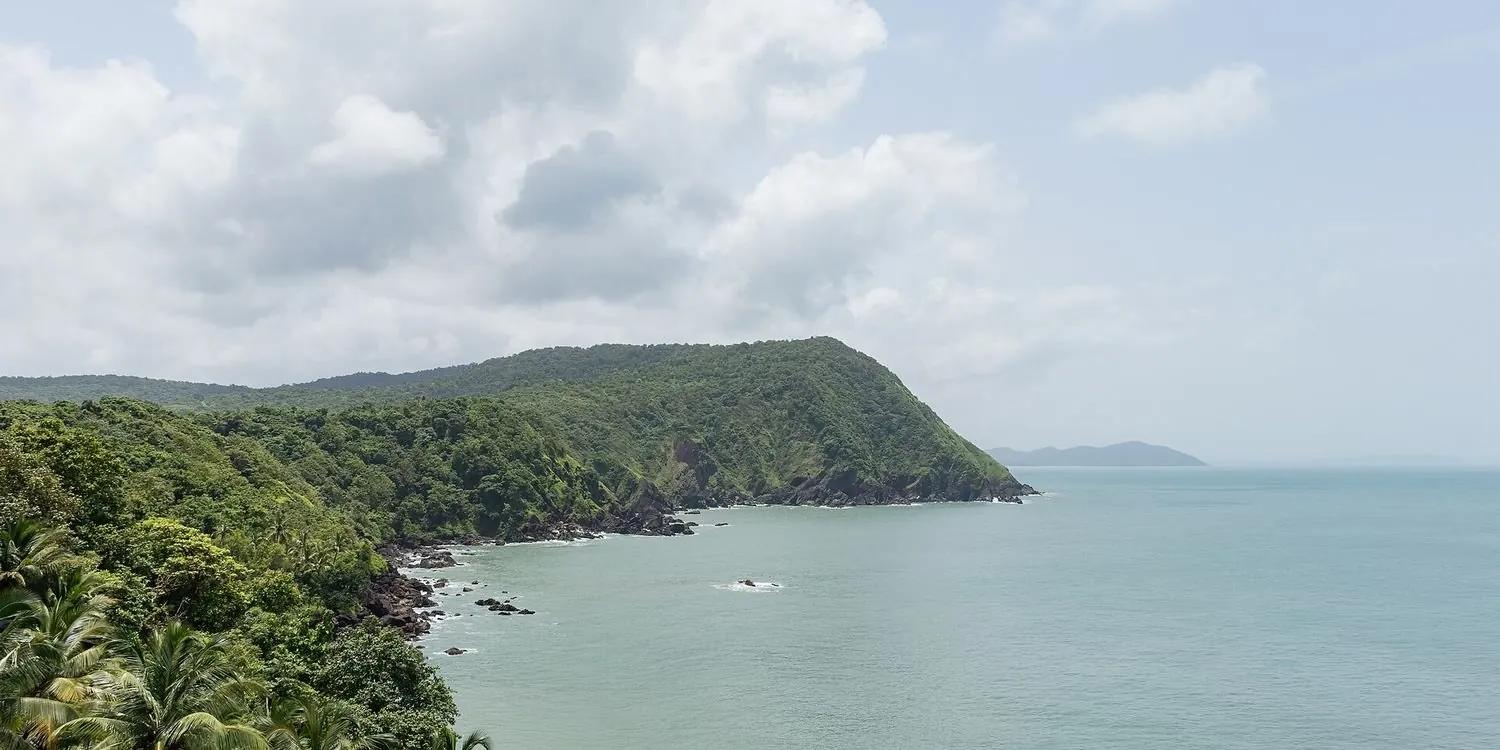 A green forested laterite headland dropping into the blue Arabian Sea, seen from Cabo de Rama Fort in South Goa