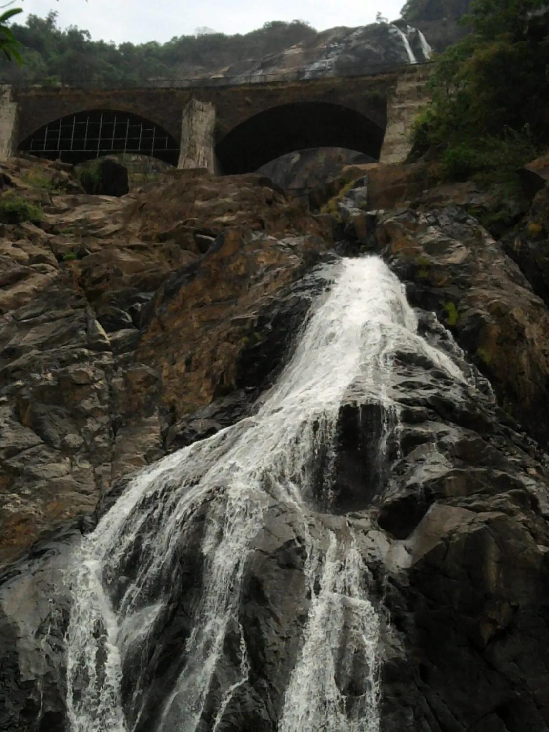 Dudhsagar Falls cascading down dark rock past the arches of an old stone railway viaduct in Goa