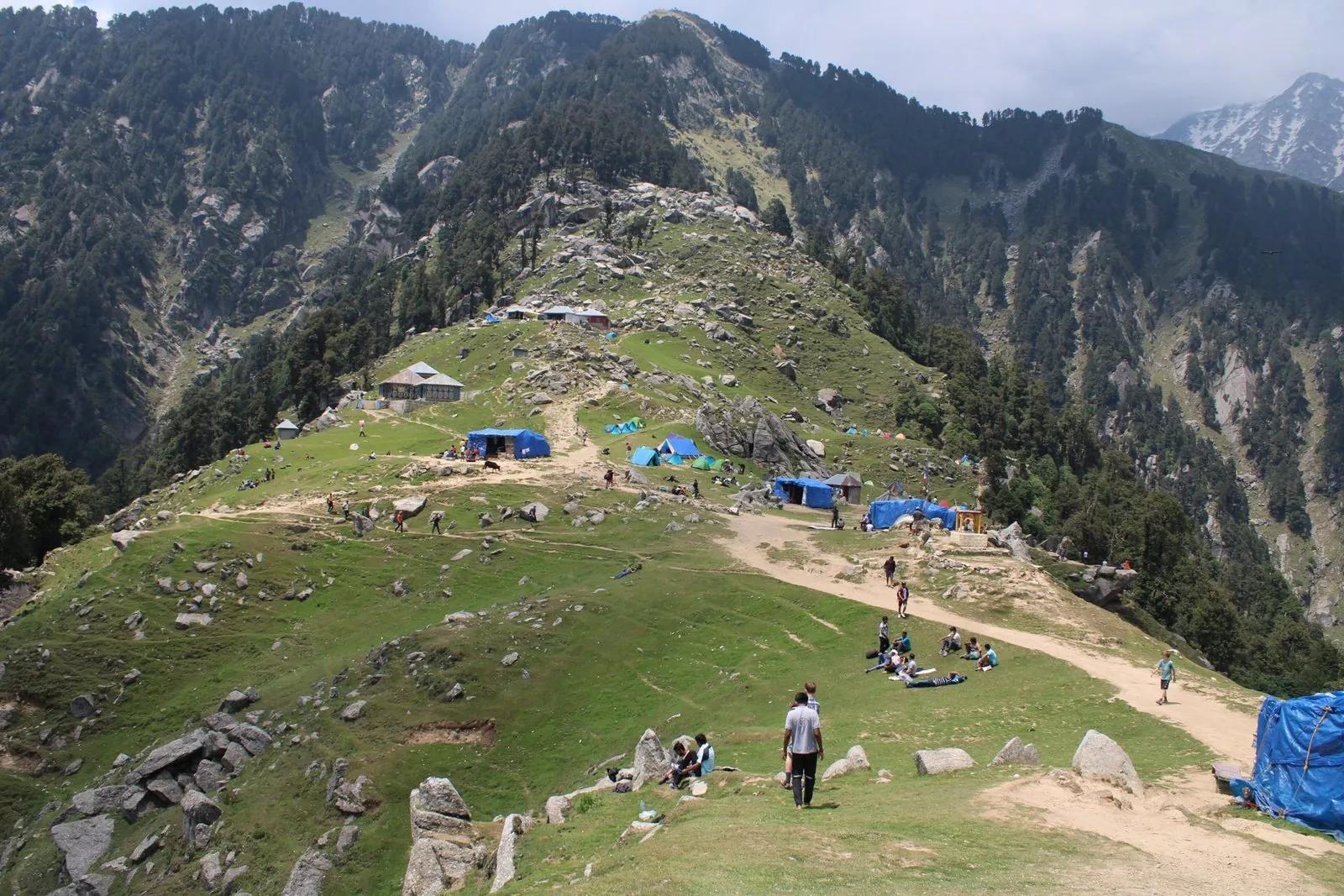 Triund summit ridge at 2,850 m with camping tents on the grassy meadow, Dhauladhar slopes behind