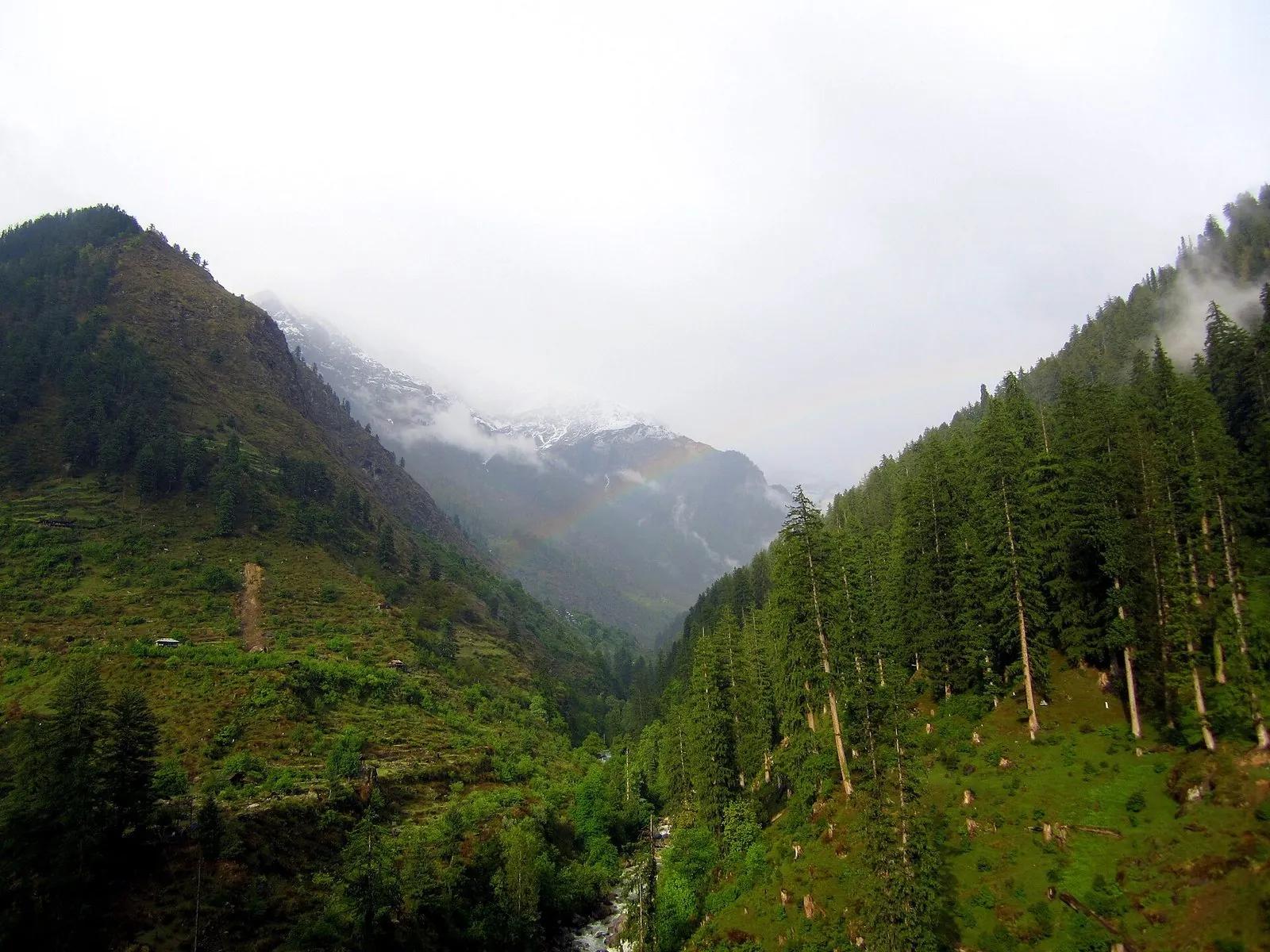 Kheerganga and Parvati Valley view with rainbow over conifer forests and snow peaks