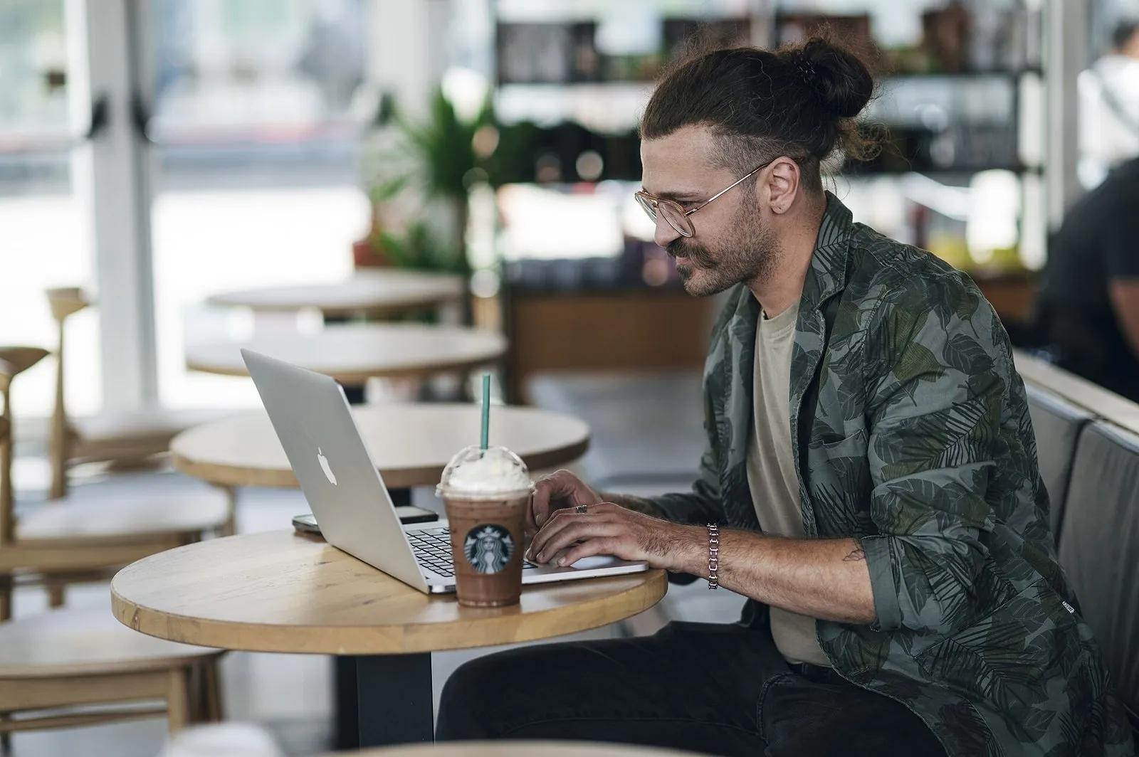 A man working on a laptop with a cold coffee in a bright cafe