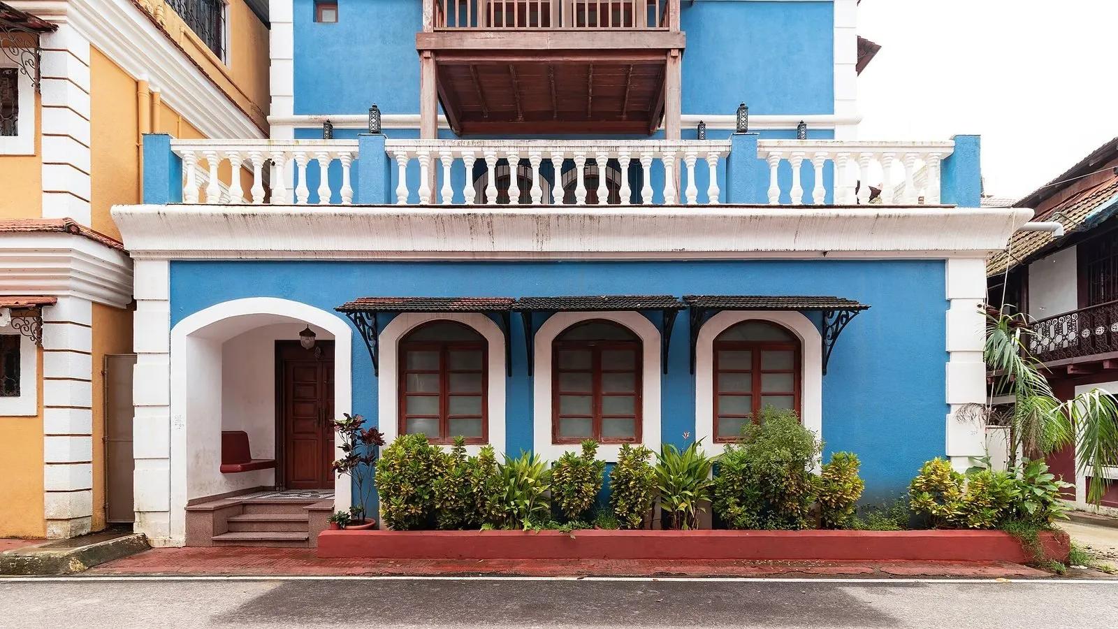 A bright blue two-storey Portuguese-era house in Fontainhas, Panjim, with a white balustraded balcony, arched windows and a tiled roof, on a quiet street.