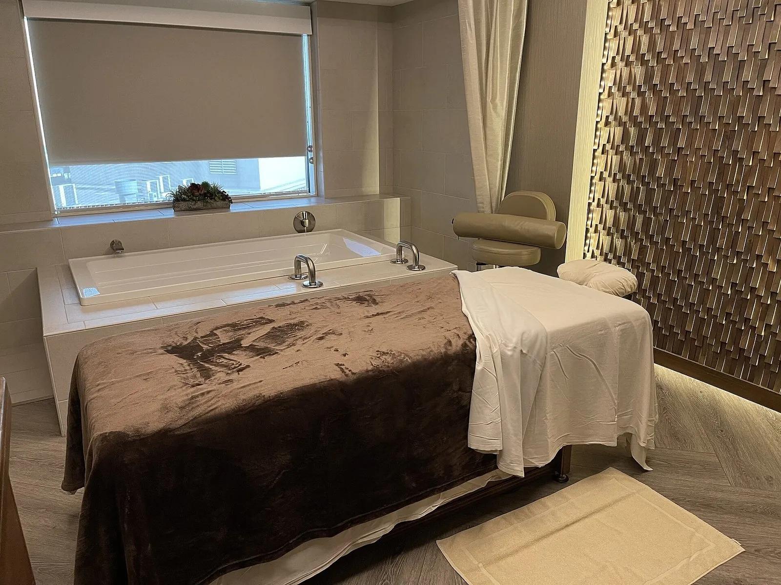 A clean, modern spa treatment room with a massage table and a soaking tub