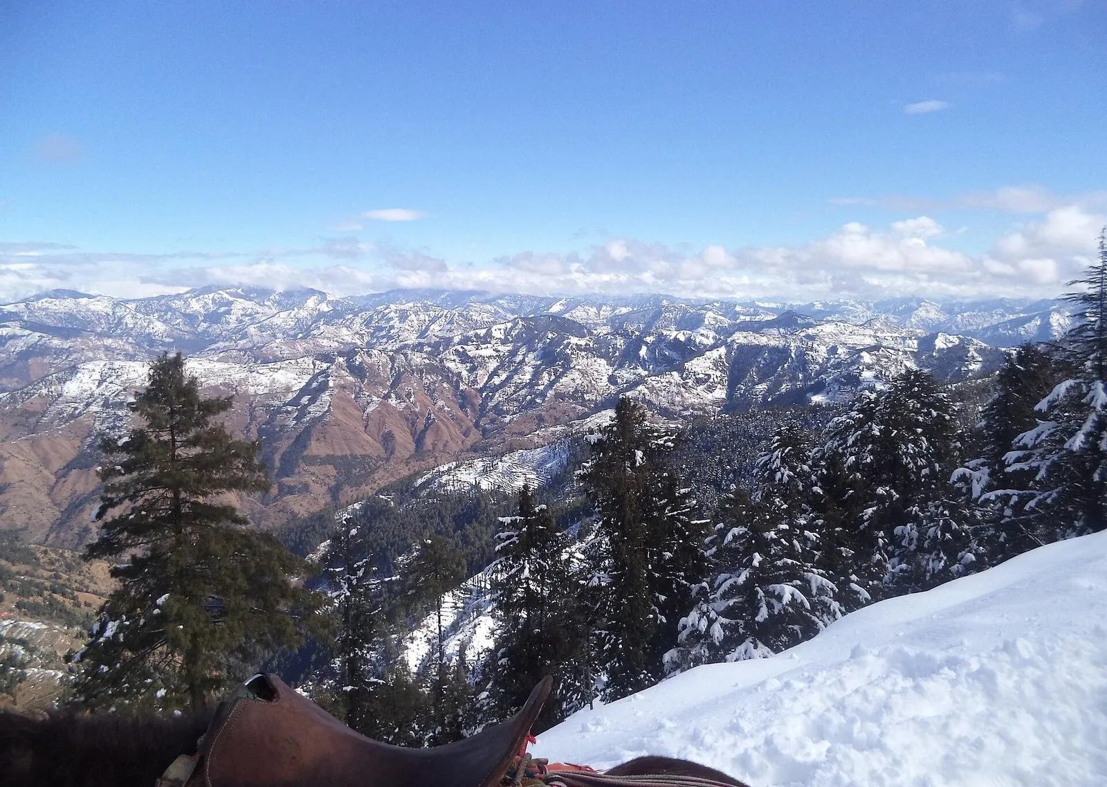 A high ridge on the edge of the Great Himalayan National Park with snow-dusted Himalayan peaks and forested valleys