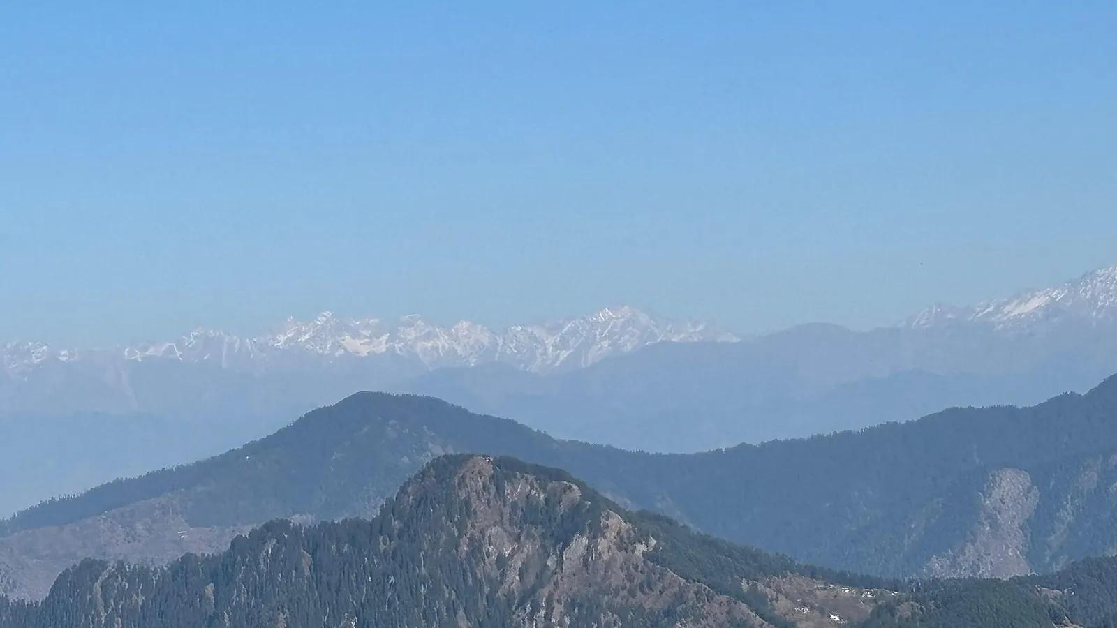 The snow-capped greater Himalaya seen across forested ridges from the summit of Shali Tibba near Shimla