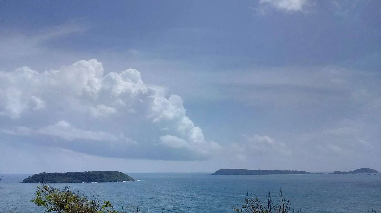 Grande Island and a smaller island sitting low on the horizon across a blue-grey sea off the Goa coast near Vasco da Gama, under a big cloudy sky.