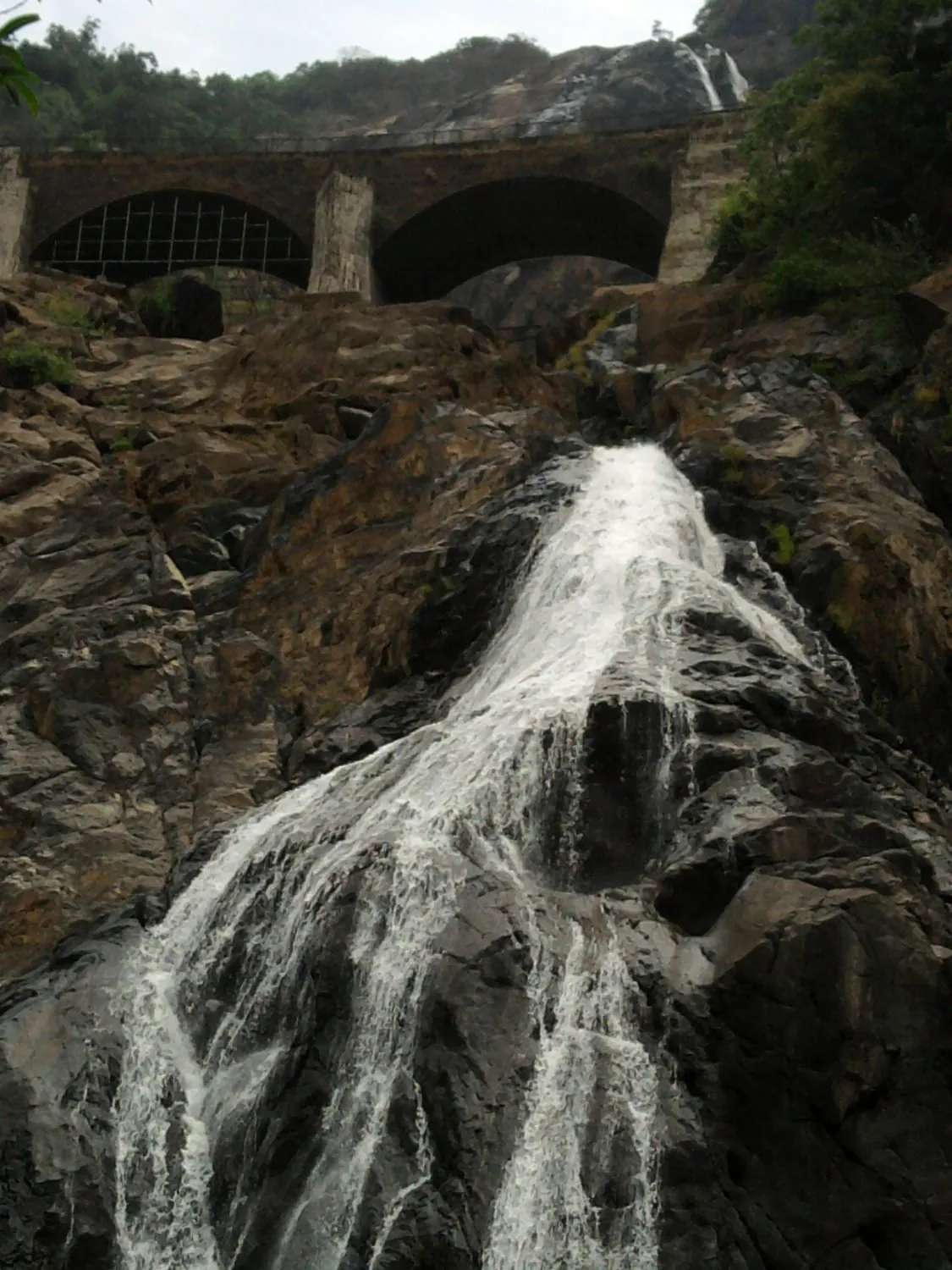 Dudhsagar Falls cascading down dark rock past the arches of an old stone railway viaduct in Goa