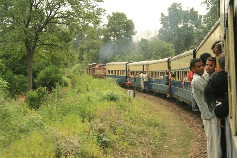 Kangra Valley narrow-gauge train winding through trees with passengers leaning out of carriages