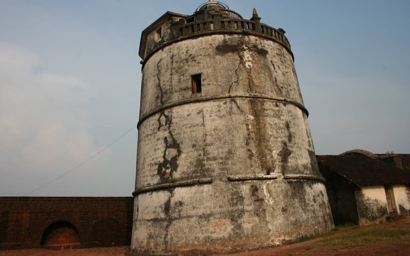 The tall round weathered lighthouse tower inside the seventeenth-century Fort Aguada in North Goa, against a pale blue sky above the laterite fort walls.