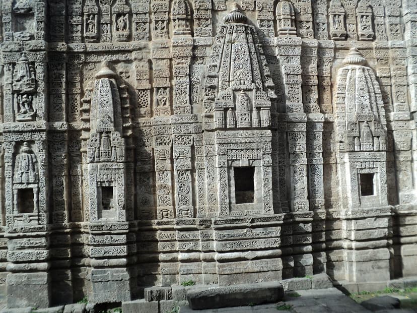 Detail of intricately carved stone temple-shrine niches set into the outer wall of Kangra Fort, with weathered relief carvings of figures and architectural ornament
