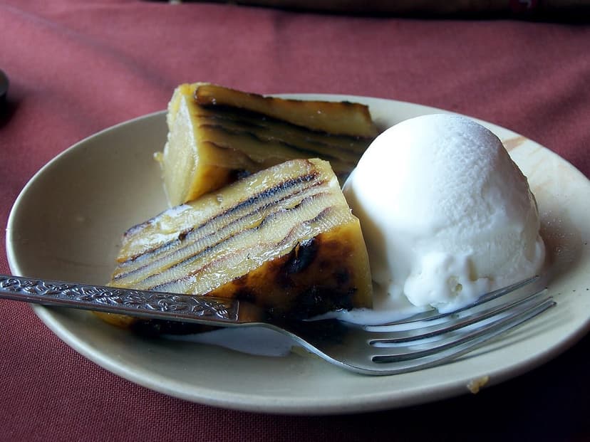 Two slices of bebinca, a golden-brown layered cake with visible thin layers, served with a scoop of vanilla ice cream