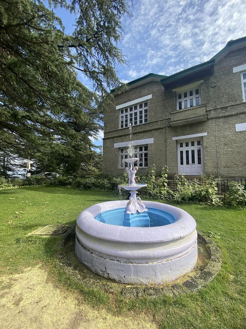 Stone fountain on the lawn of Chail Palace heritage hotel surrounded by deodar trees
