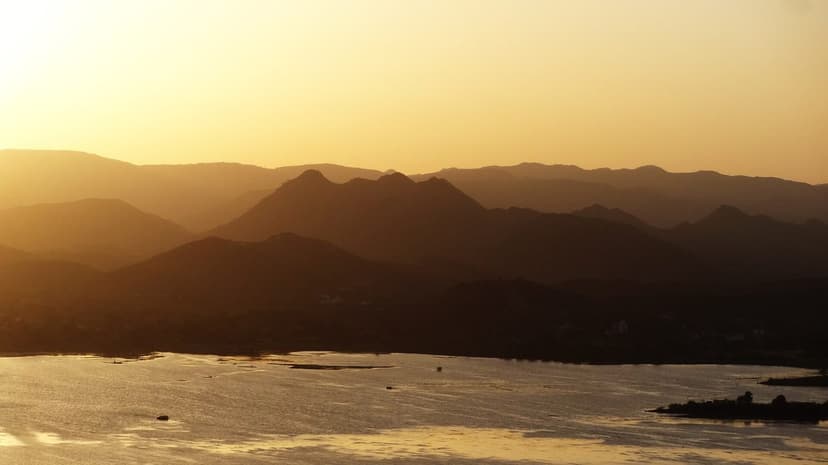 Golden sunset over a wide Udaipur lake with the Aravalli hills silhouetted in layers