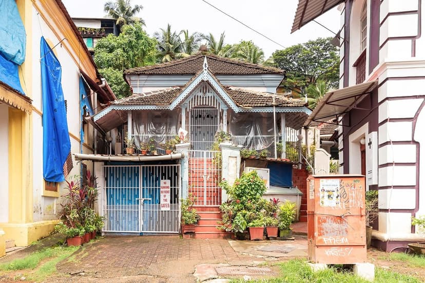 A weathered Portuguese-era house in Fontainhas, Panjim, with potted plants on red steps, a blue gate, a tarpaulin and laundry on the neighbouring buildings.