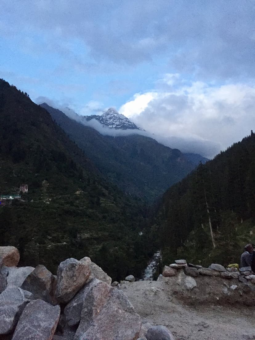 Kheerganga trek starting viewpoint with snow peak rising from clouds over stone wall