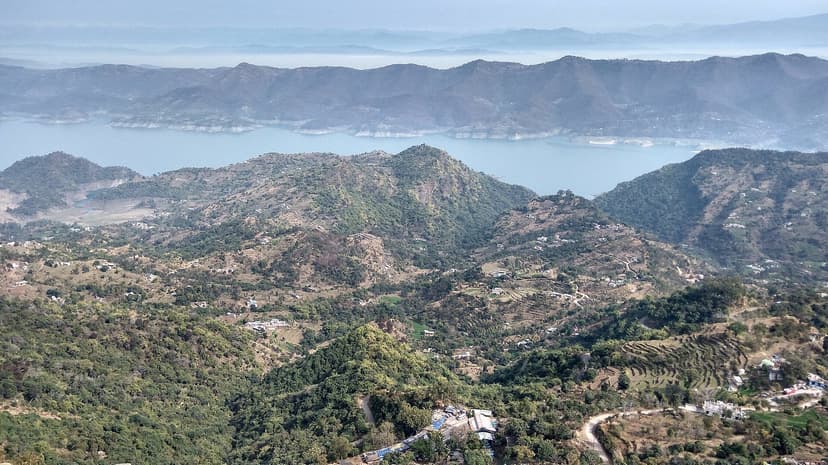 Gobind Sagar reservoir seen from the Naina Devi temple ridge, pale blue water winding between dry Shivalik hills and terraced fields