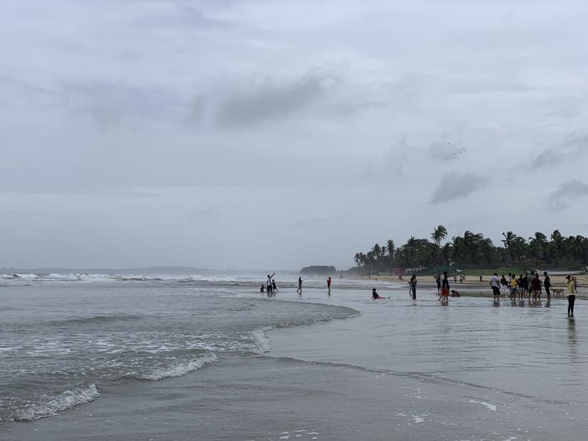 Wide Colva beach under an overcast sky with groups wading near the shoreline