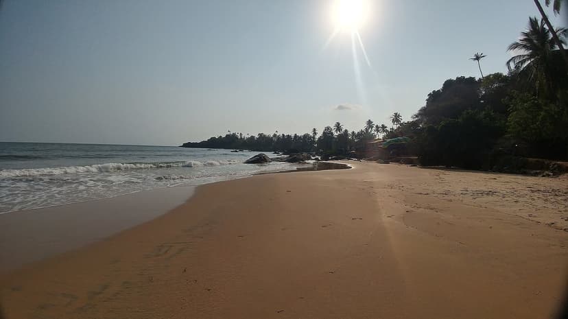 Quiet sandy curve of Patnem beach with palms, a rocky point and small beach businesses