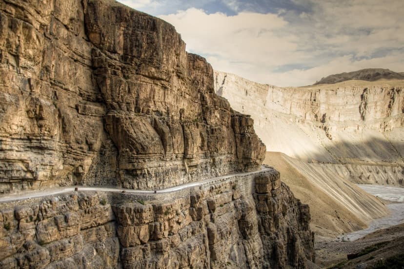 Dramatic mountain road carved into towering cliff face in the Spiti Valley, showing the scale of the landscape