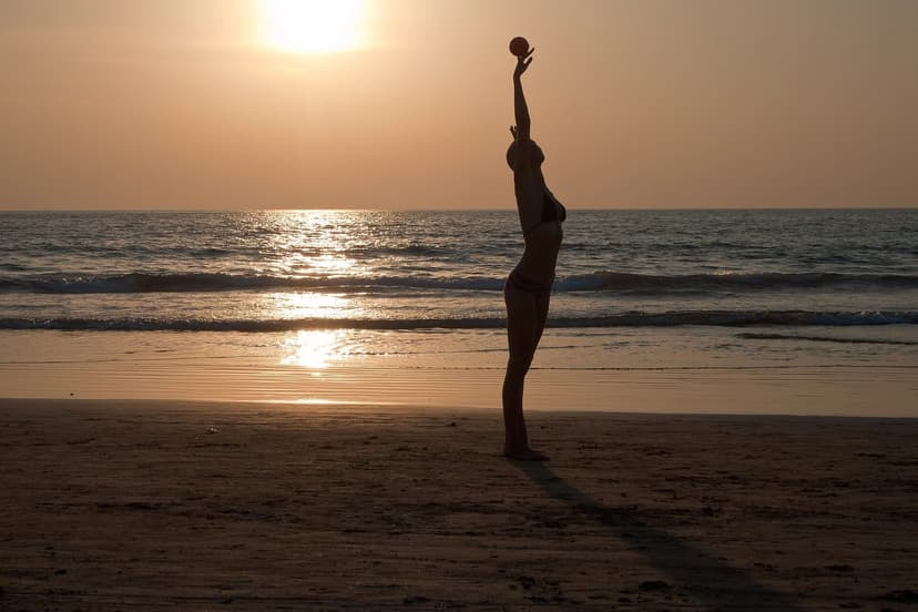 A figure in silhouette on Arambol beach at sunset reaching upward, the sun low over the sea