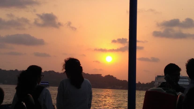 Passengers silhouetted on a river ferry deck as the sun sets over the Mandovi in Goa