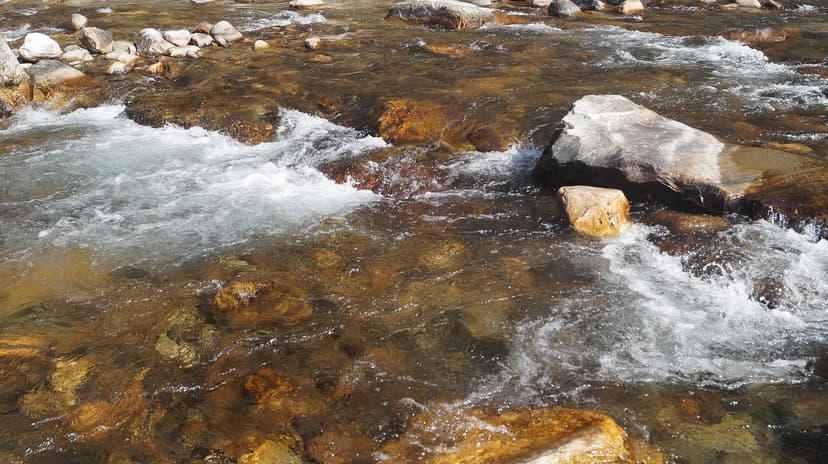Clear shallow river over orange and brown rocks with white rapids