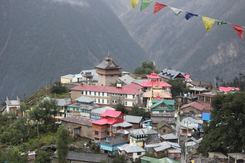 Kalpa village houses and a wooden temple tower on a forested hillside with prayer flags