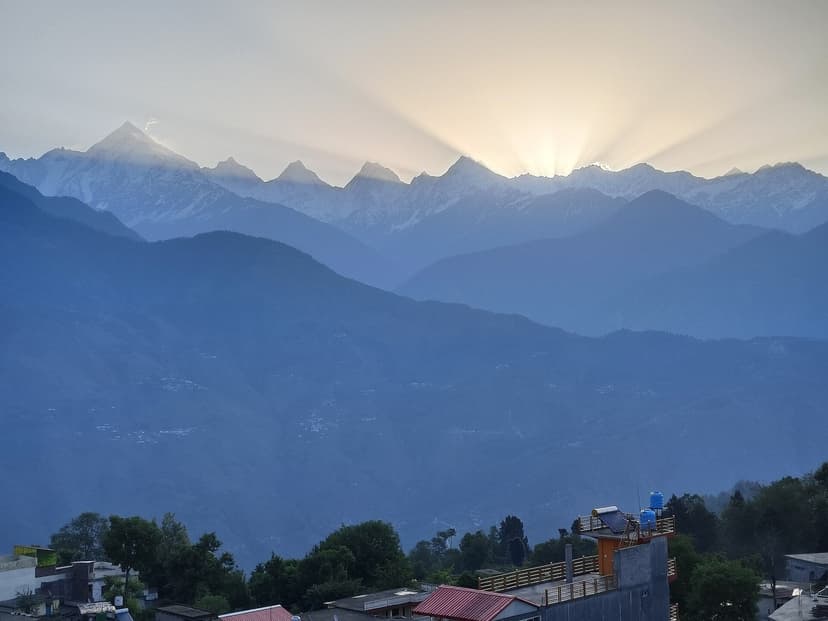Sunrise rays bursting from behind the snow-covered Panchachuli peaks with Munsiyari village rooftops in the foreground