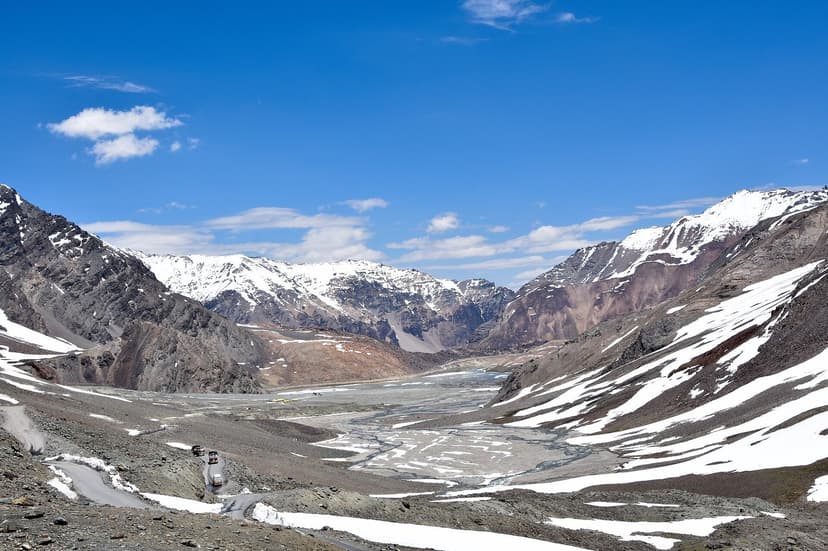 Wide panoramic view of Baralacha La pass at 4,890 metres on the Manali-Leh highway, with barren snow-streaked mountains, a wide glacial valley, and a tiny vehicle visible in the distance