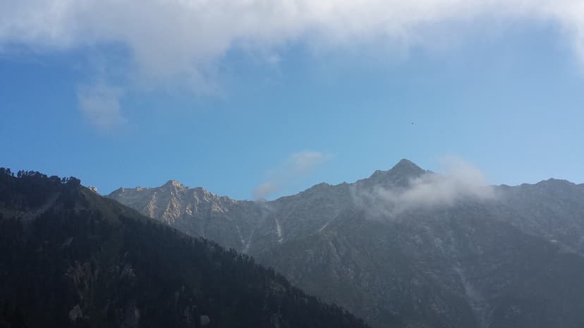 The Dhauladhar range seen from Triund campsite, bare grey-brown rock face with cloud rolling along the ridgeline and pine forest in the foreground