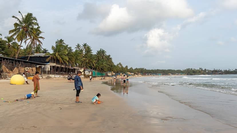 Palolem beach with palms, beach businesses and families walking along the wet sand